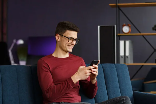 Young freelancer using smartphone and smiling. Happy man using m — Stock Photo, Image