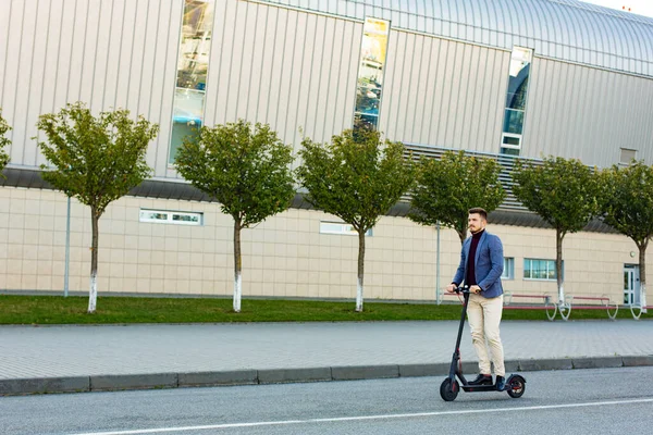 Young handsome man riding the e-scooter on the road near the airport on the sunset. Trendy urban transportation on modern electric scooter. Eco friendly mobility concept — Stock Photo, Image