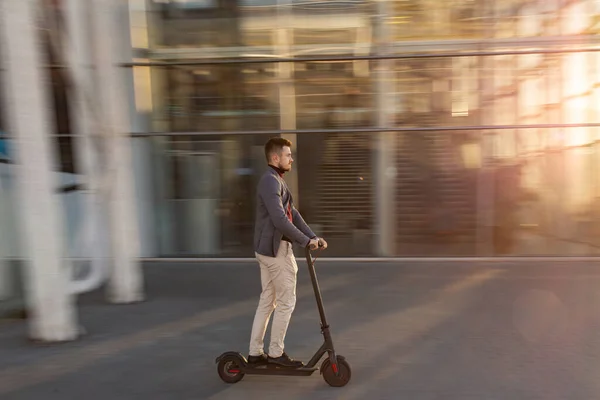 Fiatal jóképű férfi lovagol az e-robogón a reptér közelében, naplementekor. Trendi városi közlekedés modern elektromos robogóval. Környezetbarát mobilitás koncepciója — Stock Fotó