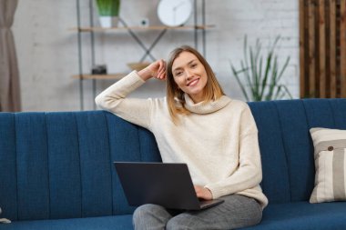 Evden çalışıyorum. Meslektaşlar ve serbest çalışanlarla çevrimiçi iletişim. Dizüstü bilgisayar kullanan ve gülümseyen genç bir kadın ressamın portresi. Mobil aygıtlarla çalışan gençlerin kavramı
