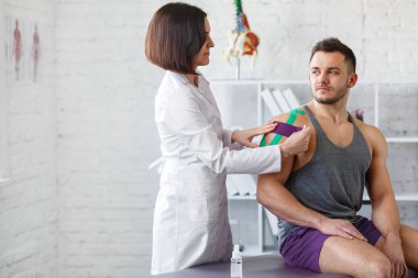 Kineziyoloji bandı. Fizyoterapist hastanın omzuna kinezyoloji bandı uyguluyor. Erkek sporcunun yaralı omzunu tedavi eden kadın terapist. Travma sonrası rehabilitasyon, spor fizyoterapisi