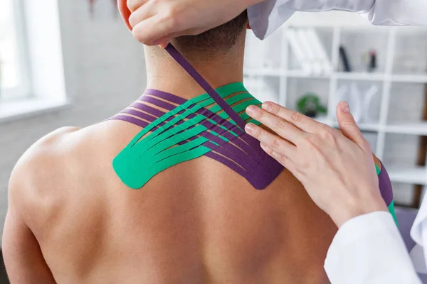 Kinesiology taping. Physical therapist applying kinesiology tape to patient neck. Therapist treating injured trapezius muscles of young athlete. Post traumatic rehabilitation, sport physical therapy — Stock Photo, Image