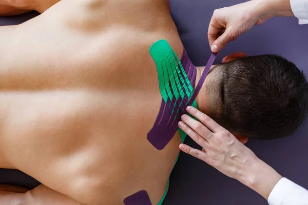 Kineziyoloji bandı. Fizyoterapist hastanın boynuna kinezyoloji bandı uyguluyor. Genç bir atletin yaralı trapezius kaslarını tedavi eden terapist. Travma sonrası rehabilitasyon, spor fizyoterapisi — Stok fotoğraf