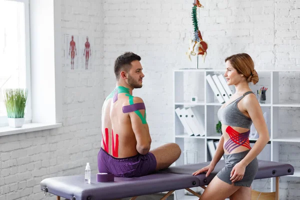 Kinesiology taping. Post traumatic rehabilitation, sport physical therapy, recovery concept. Two young male athletes visiting physiotherapist .Kinesiology tape on patient knee, shoulder,neck,hip