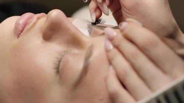 Extensiones de pestañas. Pestañas falsas. Procedimiento de extensión de pestañas. Primer plano retrato de ojo de mujer con pestañas largas. Estilista profesional que alarga las pestañas femeninas. Maestro y cliente en salón de belleza — Vídeo de stock