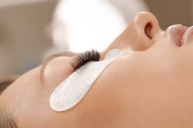 Kirpiklerini uzat. Sahte kirpikler. Kirpik uzatma prosedürü. Uzun kirpikli kadın gözünün portresini kapat. Profesyonel stilist, kadın kirpiklerini uzatıyor. Güzellik salonunda usta ve müşteri