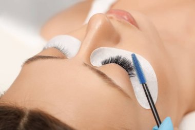 Kirpiklerini uzat. Sahte kirpikler. Kirpik uzatma prosedürü. Uzun kirpikli kadın gözünün portresini kapat. Profesyonel stilist, kadın kirpiklerini uzatıyor. Güzellik salonunda usta ve müşteri
