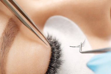 Kirpiklerini uzat. Sahte kirpikler. Kirpik uzatma prosedürü. Uzun kirpikli kadın gözünün portresini kapat. Profesyonel stilist, kadın kirpiklerini uzatıyor. Güzellik salonunda usta ve müşteri