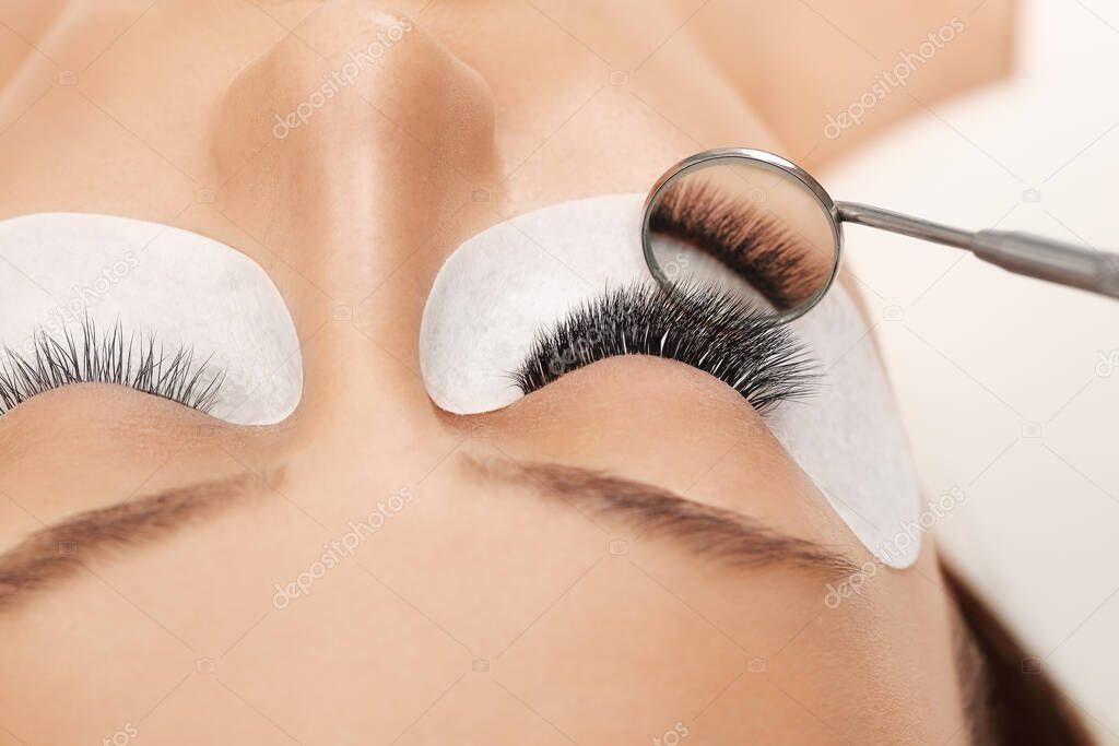 Eyelashes extensions. Fake eyelashes. Eyelash extension procedure.Close up portrait of woman eye with long eyelashes. Professional stylist lengthening female lashes. Master and client in beauty salon