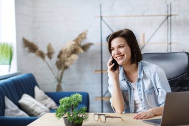 Evden çalışıyorum. Meslektaşlarım ve serbest çalışanlarımla internet üzerinden iletişim kuruyorum. Akıllı telefondan konuşan ve gülümseyen genç bir kadın ressamın portresi. Mobil aygıtlarla çalışan gençlerin kavramı