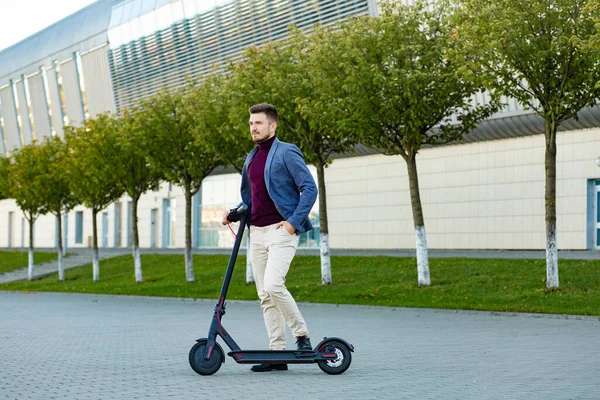 Junger gutaussehender, stilvoller Mann mit E-Scooter, der bei Sonnenuntergang auf dem Bürgersteig in der Nähe des Flughafens steht. trendige Stadtverkehr auf modernen Elektroroller. Umweltfreundliches Mobilitätskonzept — Stockfoto