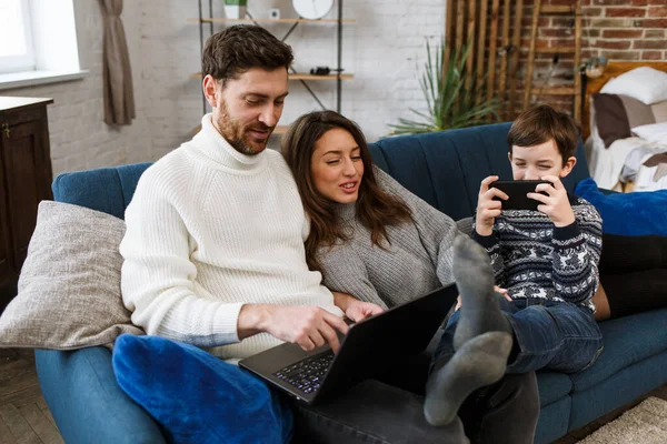 Mother, father and son using laptop and mobile phones at home. Family members ignoring each other and live talk. Gadget influence on family relationships. Modern technologies and addiction concept