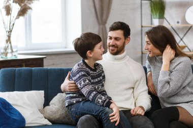 Gülümseyen baba, anne ve oğul portresi. Mutlu aile evde birlikte vakit geçiriyor. Evde anne ve babasıyla oynayan tatlı çocuk. Aile eğlencesi zamanı. Aile değerleri