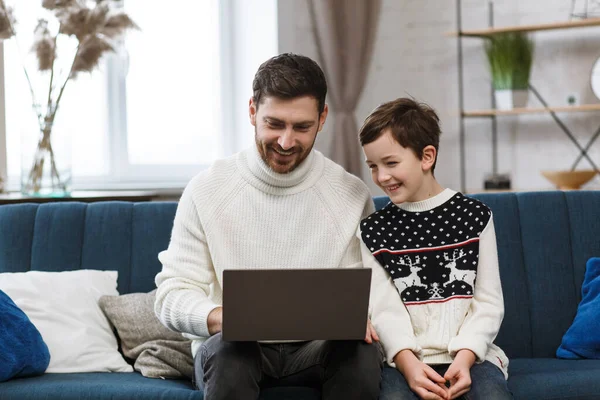 Quédate en casa. Retrato de padre e hijo sonrientes usando un portátil para una reunión en línea, videollamada, videoconferencia con familiares, educación en el hogar. Feliz familia pasando tiempo juntos en casa —  Fotos de Stock