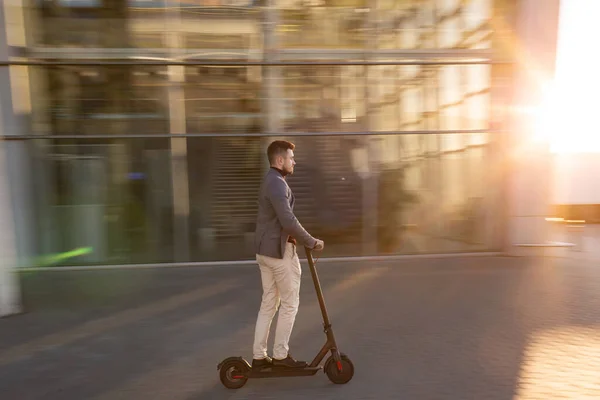 Fiatal jóképű férfi lovagol az e-robogón a reptér közelében, naplementekor. Trendi városi közlekedés modern elektromos robogóval. Környezetbarát mobilitás koncepciója — Stock Fotó