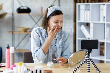 Genç bayan blogcu güzellik blogu için kozmetik hakkında özel bir video kaydediyor. Vlogger yüz kremini test ediyor ve sosyal ağda canlı yayın yapıyor. Bloglama, video bloglama, cilt bakımı konsepti