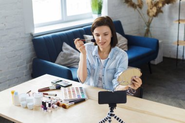 Genç bayan blogcu güzellik blogu için kozmetik hakkında özel bir video kaydediyor. Vlogger yüz pudrasını test ediyor ve sosyal ağda canlı yayın yapıyor. Bloglama, video bloglama, makyaj konsepti