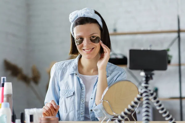 Young female blogger recording a tutorial video for her beauty blog about cosmetics.Vlogger testing eye pads and broadcast live video to social network at home. Blogging, videoblog, skincare concept