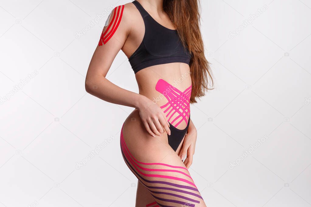 Kinesiology taping. Young female athlete on white background with kinesiology tape on tummy and hips. Fat lose, cellulite removal, sport physical therapy,recovery concept