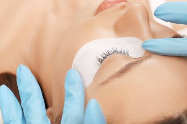 Kirpiklerini uzat. Sahte kirpikler. Kirpik uzatma prosedürü. Uzun kirpikli kadın gözünün portresini kapat. Profesyonel stilist, kadın kirpiklerini uzatıyor. Güzellik salonunda usta ve müşteri