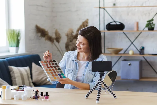 Young female blogger recording a tutorial video for her beauty blog about cosmetics.Vlogger testing eyeshadow and broadcast live video to social network at home.Blogging, videoblog, makeup concept