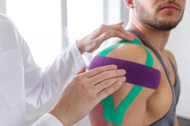 Kinesiology taping. Physical therapist applying kinesiology tape to patient shoulder. Female therapist treating injured shoulder of male athlete. Post traumatic rehabilitation, sport physical therapy clipart