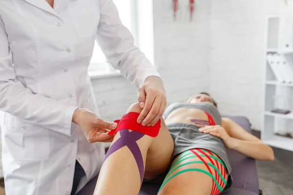 Kinesiology taping.Physical therapist applying kinesiology tape to patient knee.Therapist treating injured knee of young athlete.Post traumatic rehabilitation, sport physical therapy,recovery concept