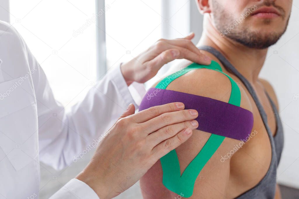 Kinesiology taping. Physical therapist applying kinesiology tape to patient shoulder. Female therapist treating injured shoulder of male athlete. Post traumatic rehabilitation, sport physical therapy
