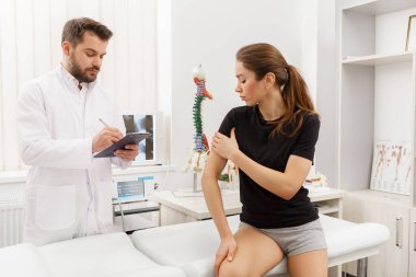 Erkek doktor, dirsek ağrısı çeken kadın hastayı muayene ediyor. Tıbbi muayene. Kayropraktik, osteopati, travma sonrası rehabilitasyon, spor fizyoterapisi. Alternatif tıp, ağrı kesici kavramı