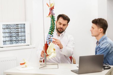 Doktor, hastasına esnek omurga modeli gösteriyor ve muayenehanedeki ağrısının nedenini açıklıyor. Klinikteki fizyoterapisti ziyaret eden hasta. Cerrahi, sağlık ve tıp konsepti