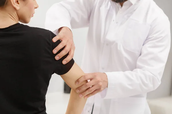 Mannelijke arts onderzoekt vrouwelijke patiënt die lijdt aan elleboogpijn. Medisch onderzoek. Chiropractie, osteopathie, posttraumatische revalidatie, sport fysiotherapie. Alternatieve geneeskunde, pijn verlichting concept — Stockfoto