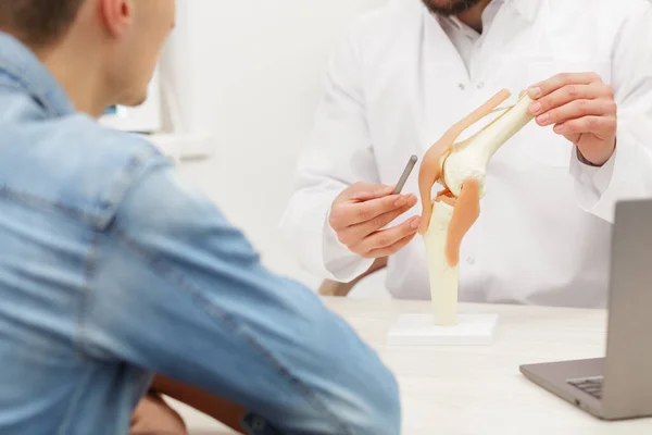 Lekarz pokazuje pacjentowi elastyczny model stawu kolanowego i wyjaśnia przyczynę bólu w gabinecie medycznym. Pacjent odwiedzający fizjoterapeutę w klinice. Koncepcja chirurgii, opieki zdrowotnej i medycyny — Zdjęcie stockowe