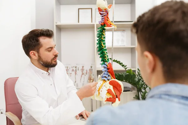 Lekarz pokazuje pacjentowi elastyczny model kręgosłupa i wyjaśnia przyczynę bólu w gabinecie medycznym. Pacjent odwiedzający fizjoterapeutę w klinice. Koncepcja chirurgii, opieki zdrowotnej i medycyny — Zdjęcie stockowe