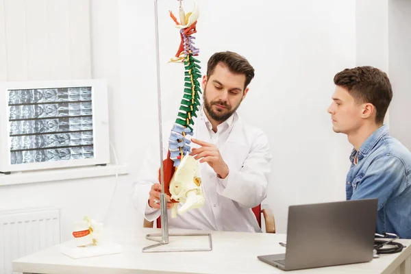 Doctor mostrando modelo de columna flexible a su paciente y explica la causa de su dolor en el consultorio médico. Paciente que visita a fisioterapeuta en clínica. Concepto de cirugía, salud y medicina —  Fotos de Stock