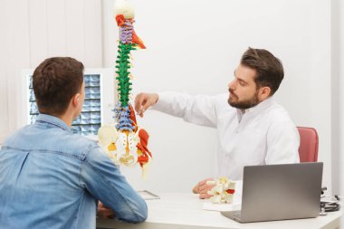 Doktor, hastasına esnek omurga modeli gösteriyor ve muayenehanedeki ağrısının nedenini açıklıyor. Klinikteki fizyoterapisti ziyaret eden hasta. Cerrahi, sağlık ve tıp konsepti