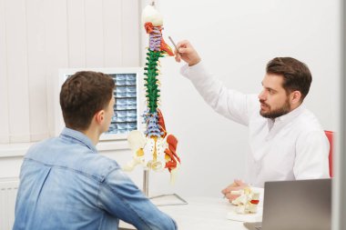 Doktor, hastasına esnek omurga modeli gösteriyor ve muayenehanedeki ağrısının nedenini açıklıyor. Klinikteki fizyoterapisti ziyaret eden hasta. Cerrahi, sağlık ve tıp konsepti