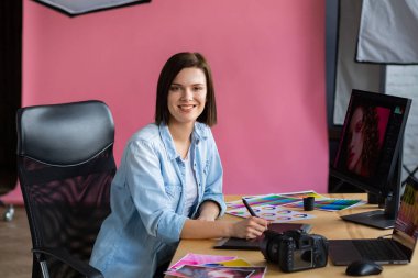 Ofiste dizüstü bilgisayar, monitör, grafik çizim tableti ve renk paleti ile çalışan grafik tasarımcısının portresi. Özel programda resimler alınıyor. Fotoğraf stüdyosunda iş yeri alınıyor. Yaratıcı ajans