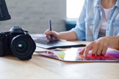 Grafik tasarımcı ellerinin özel programda grafik çizim tableti kullanarak resimleri rötuşladığı portreyi kapat. Laptop, monitör ve renk paleti. Fotoğraf stüdyosundaki işyerinde. Yaratıcı ajans