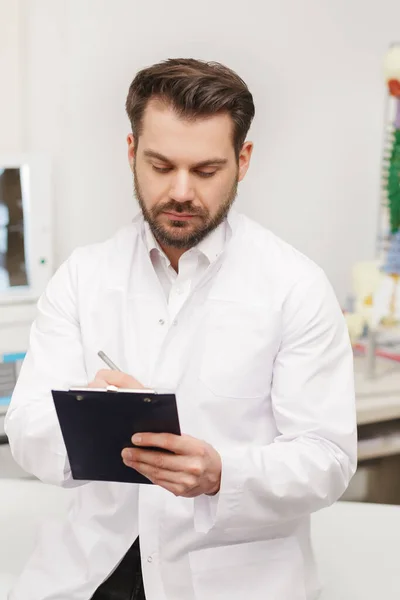 Portrait of doctor in white coat at workplace with medical staff on the background. Male doctor working at office desk. Medical office, clinic