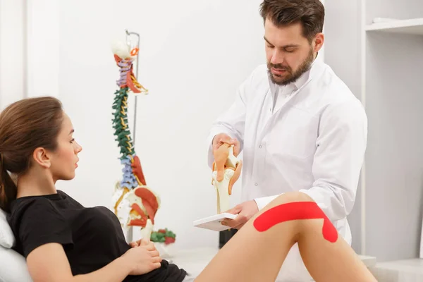 Cinta de cinesiología.Fisioterapeuta que aplica cinta de cinesiología a la rodilla del paciente.Terapeuta que trata la rodilla lesionada del atleta jóvene.Rehabilitación postraumática, terapia física deportiva, concepto de recuperación —  Fotos de Stock