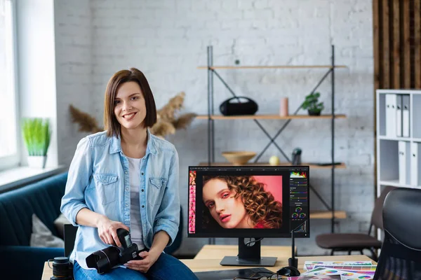 Portret van een professionele fotograaf met camera in de fotostudio. Werkplaats in het kantoor met camera, laptop, monitor, grafische tablet en kleurenpalet. Terugtrekken van beelden. Creatief agentschap — Stockfoto