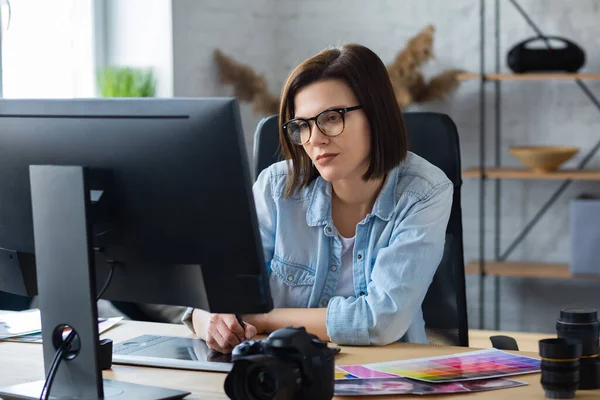 Portret van grafisch ontwerper die werkt in het kantoor met laptop, monitor, grafische tablet en kleurpalet.Retoucheren van beelden in speciaal programma.Retoucher werkplek in fotostudio.Creative agency — Stockfoto