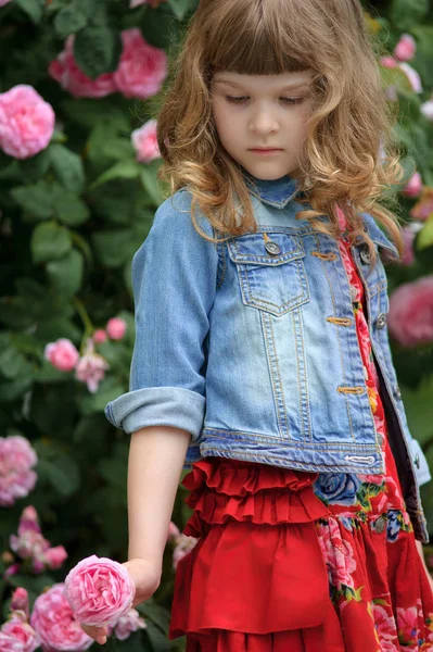 Enfant fille en robe rouge jouant avec des roses dans le jardin d'été — Photo