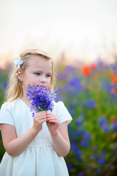 Bela jovem loira no campo verde com flores — Fotografia de Stock