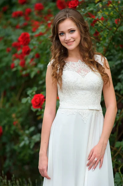Bir gül bahçesinde poz beyaz bir elbise genç güzel kadın