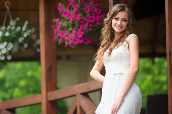 Sorrindo jovem mulher em vestido branco posando perto da varanda da casa com — Fotografia de Stock