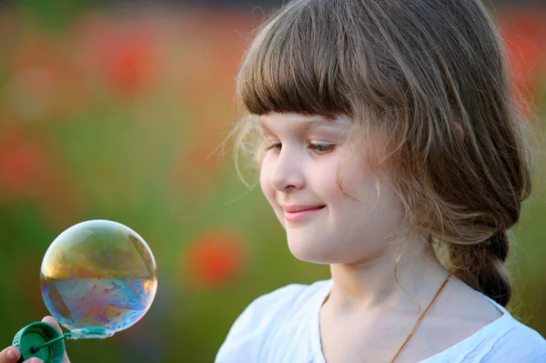 A little girl blowing soap bubbles in summer park — Stock Photo, Image