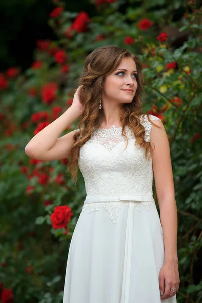 smiling beautiful young woman wearing white dress near blooming