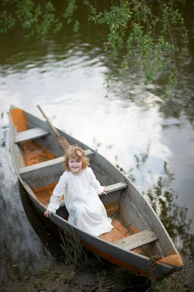 Petit enfant assis dans le bateau à la rivière. Enfant portant du blanc — Photo