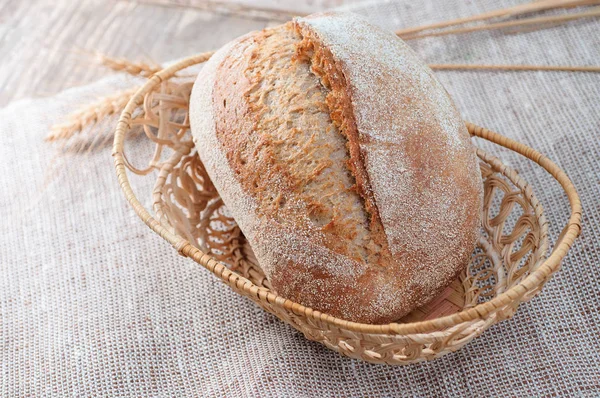 Pagnotta di pane su un piattino di vimini con sfondo in legno . — Foto Stock